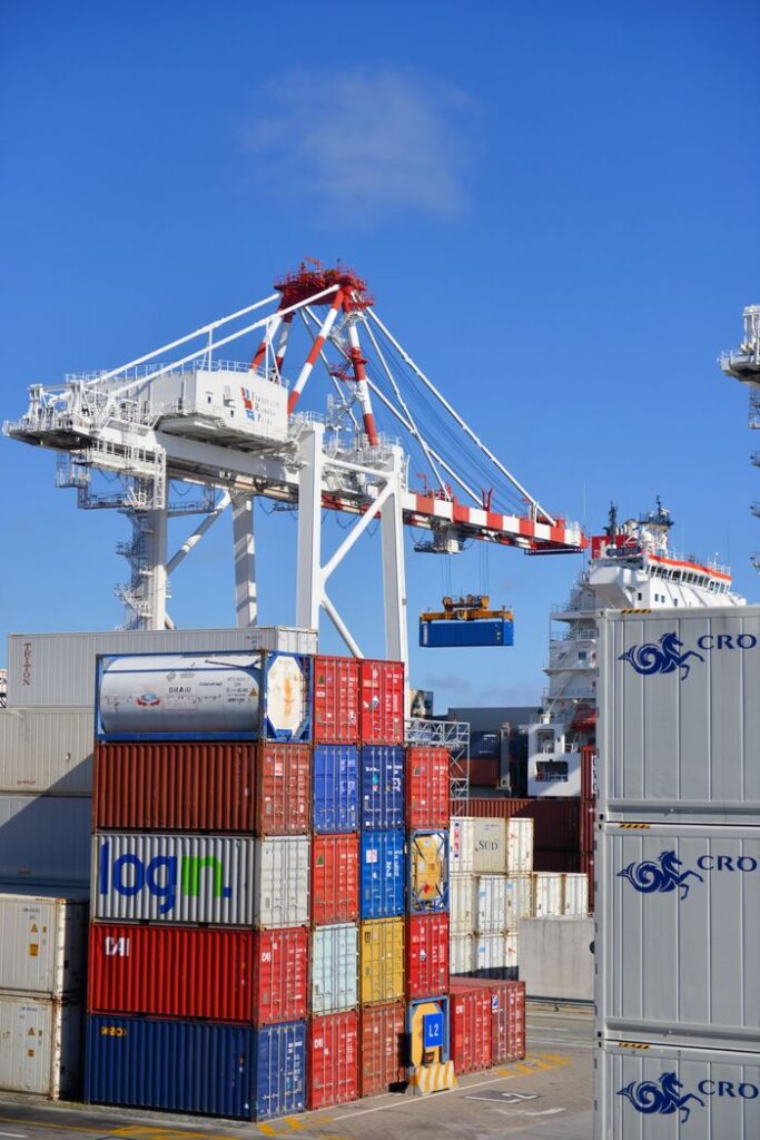 Colorful shipping containers stacked in a busy port with cranes overhead.
