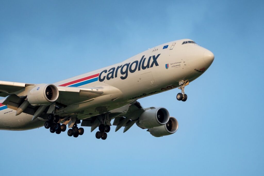 A Cargolux cargo plane flies against a clear blue sky, showcasing its massive structure.